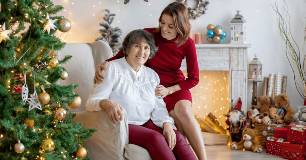 Senior mom with adult daughter by the Christmas tree for the holidays and presents and decorations in the background